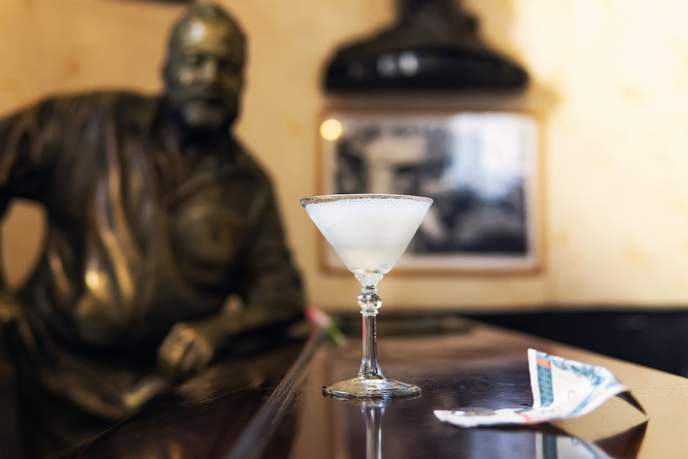 The Ultimate Cuba Bucket List: 101 Fun Things To Do in Cuba. Picture of frozen daiquiri and statue of famous American writer, Ernest Hemingway in the bar El Floridita in Havana, Cuba. 