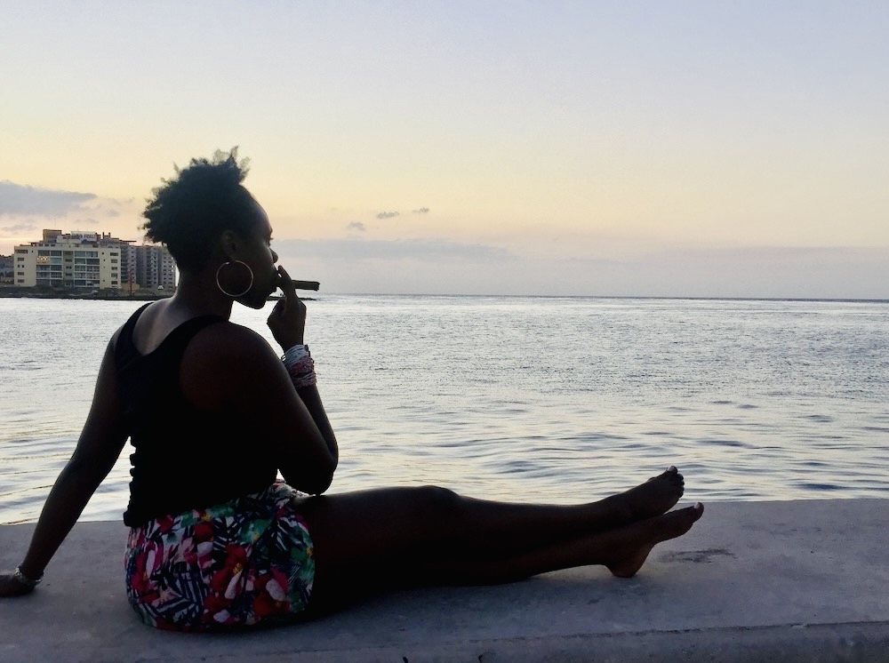 Complete travel guide for first time visitors.  Lady Chin smoking a cigar and sitting at the Malecon in Havana, Cuba. 