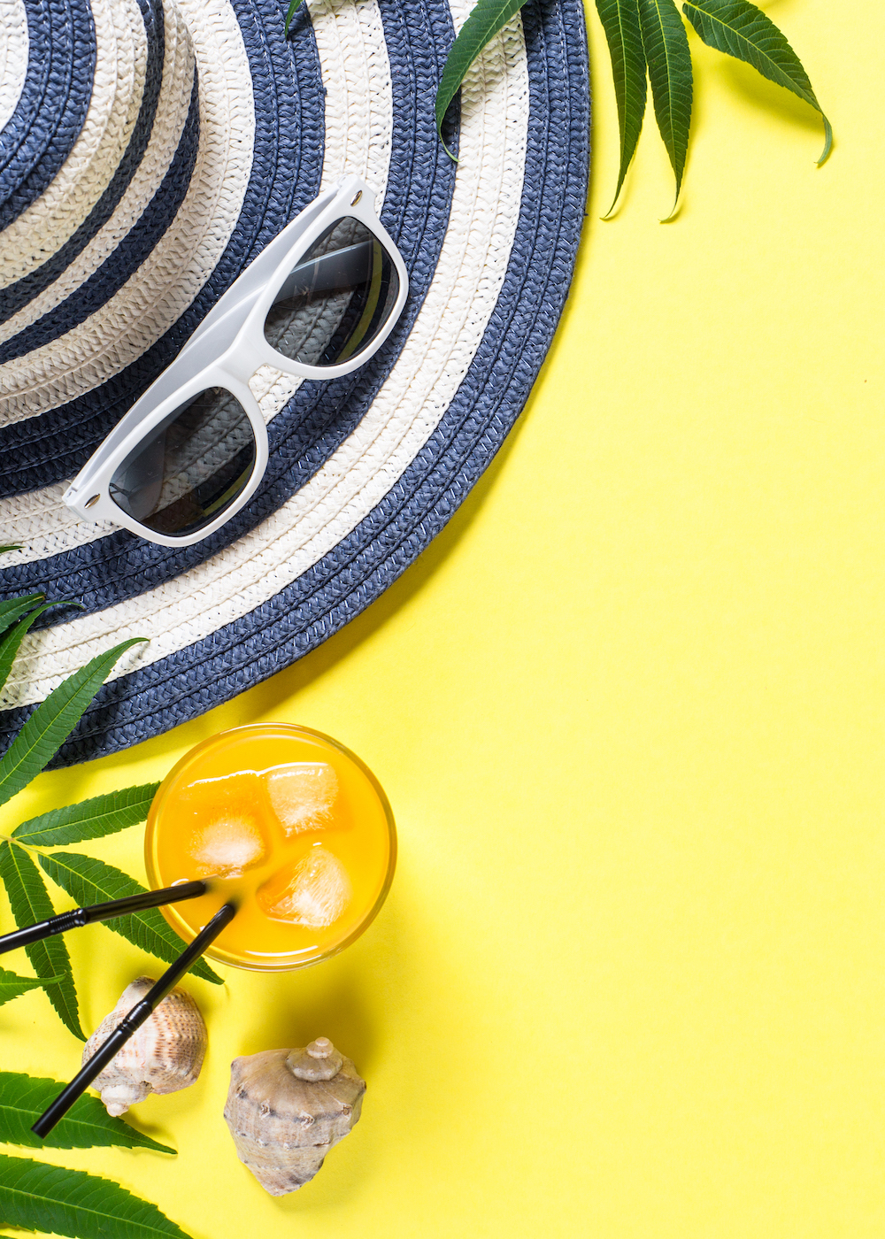 Summer travel vacation essentials. Striped hat, drink and tropical vibes with yellow background. 