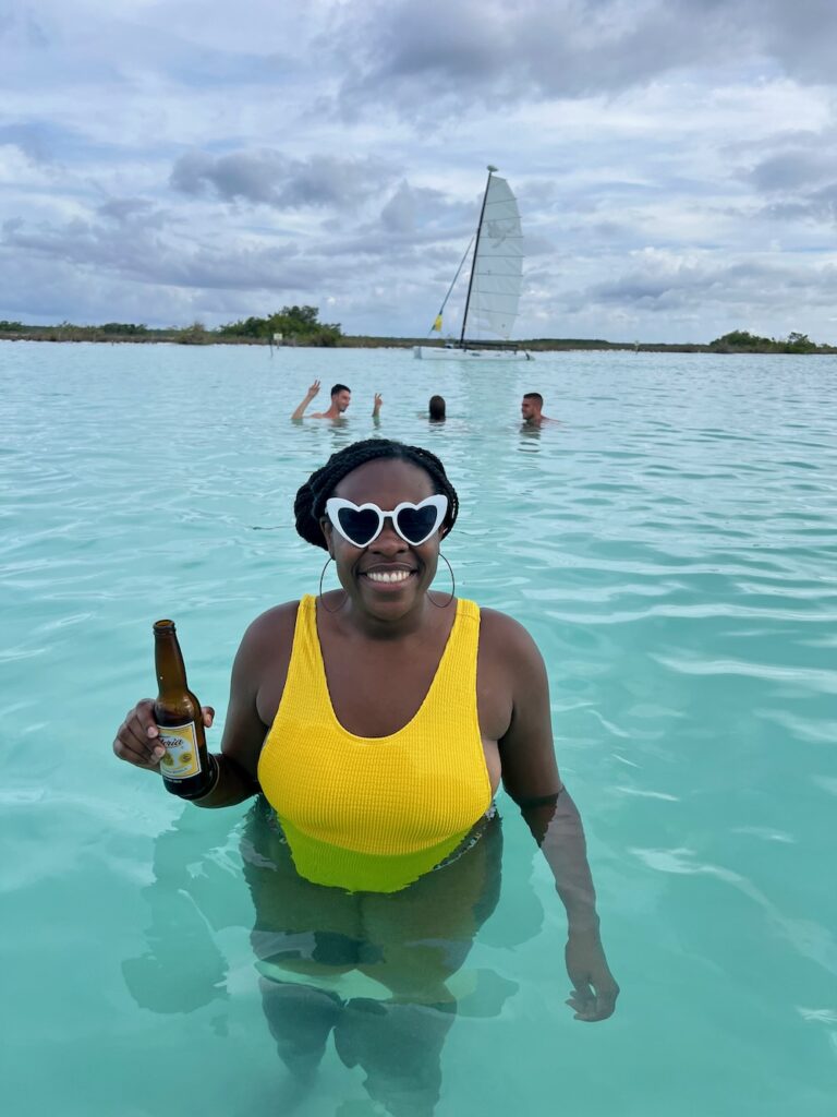 A Black women wearing a yellow bathing suit holding a beer in the Bacalar Lagoon, Mexico.