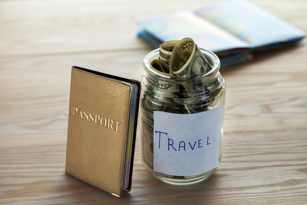 Passport and a glass jar labeled travel filled with money on a wooden background for financing work and travel. 