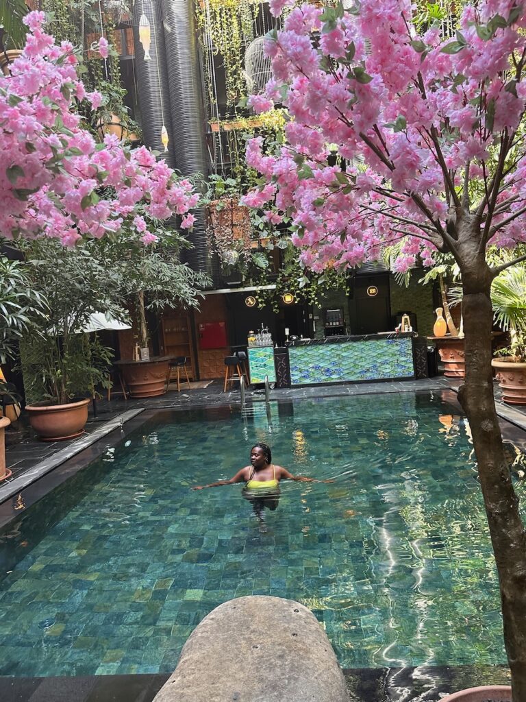 Pretty Black woman in a Bali-style swimming pool with lush green plants and tiled bar embracing the perks of work and travel. 