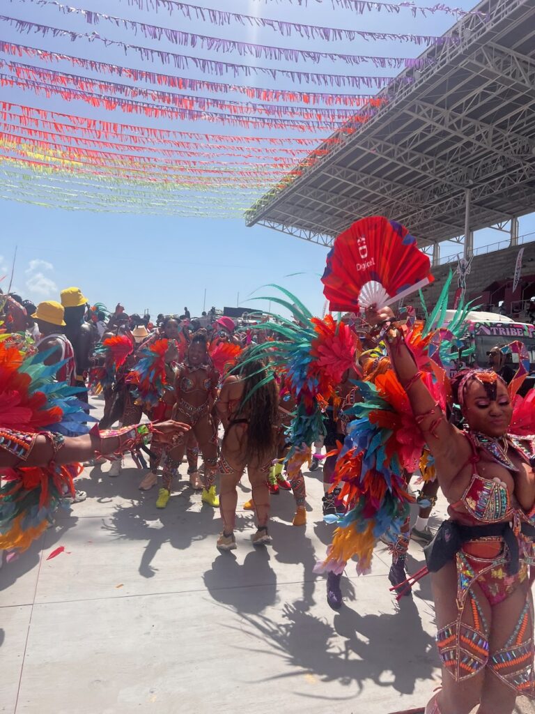 Happy masqueraders wearing colorful costumes with feathers on a sunny day crossing the Socadrome stage in Port of Spain, Trinidad. 