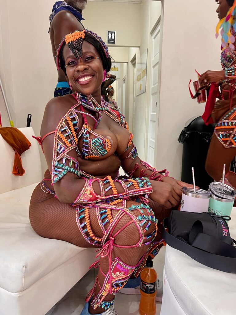 Pretty Black lady smiling while sitting down dressed in a stunning costume for Trinidad Carnival. 