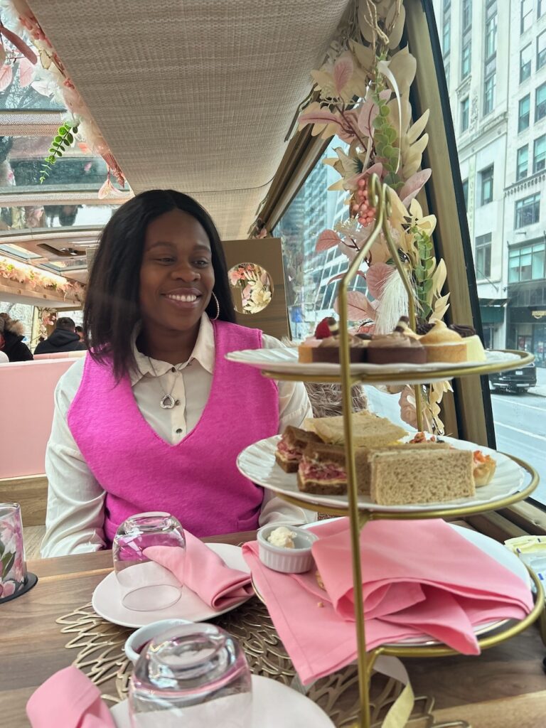 Black lady smiling down wearing a pink top with white shirt with a tray of tea sandwiches. Tea round town in NYC.  Travel with a Full-Time Job guide. 