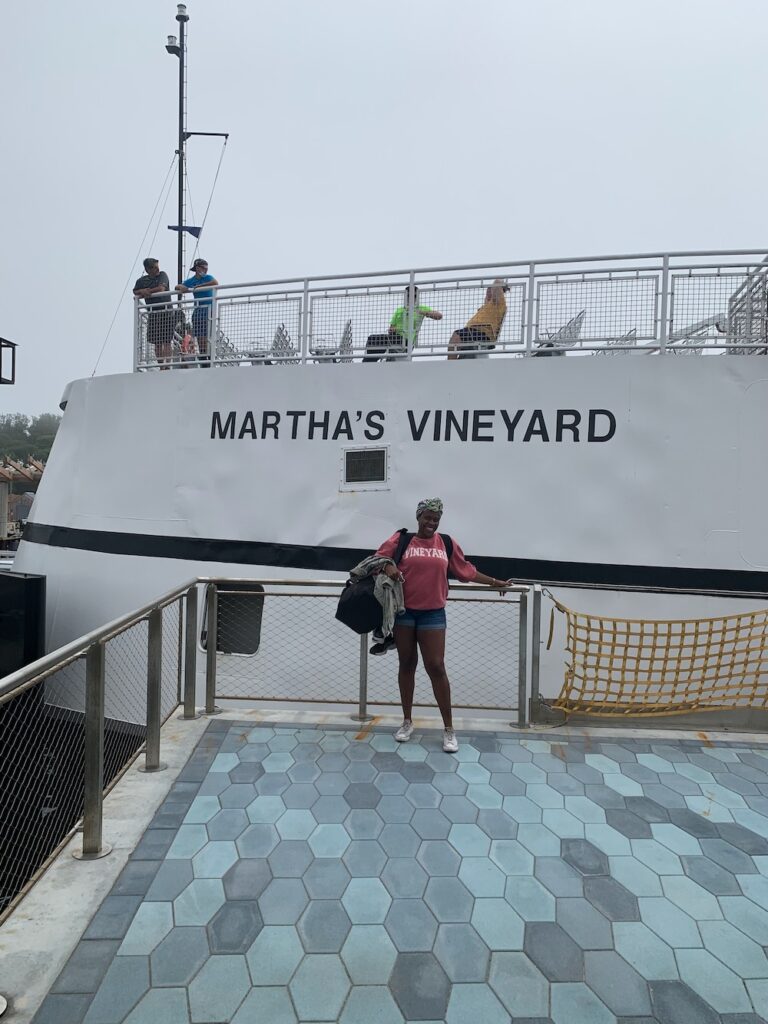 Black women in pink sweat shirt and shorts standing in front of the steamship authority with Martha's Vineyard sign on the ferry. 