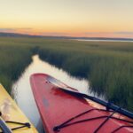 Red kayak in mash with sunset in the distance. 