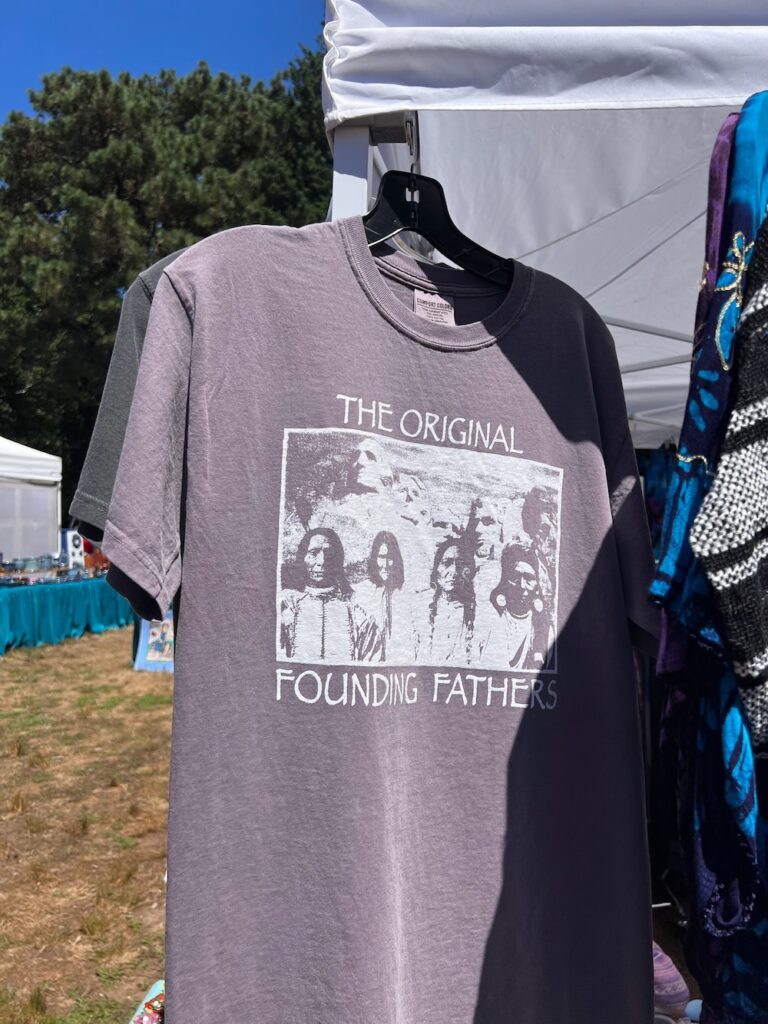 Dark T-shirt with native Americans on the front of Mt. Rushmore with the words: The Original Founding Fathers at Chilmark fair in Martha's Vineyard.