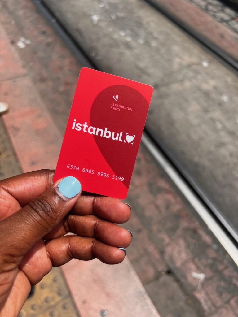 Black lady with blue nail polish holding a red Istanbulkart.  It's necessary to get if you're visiting Istanbul for first time visitors. 