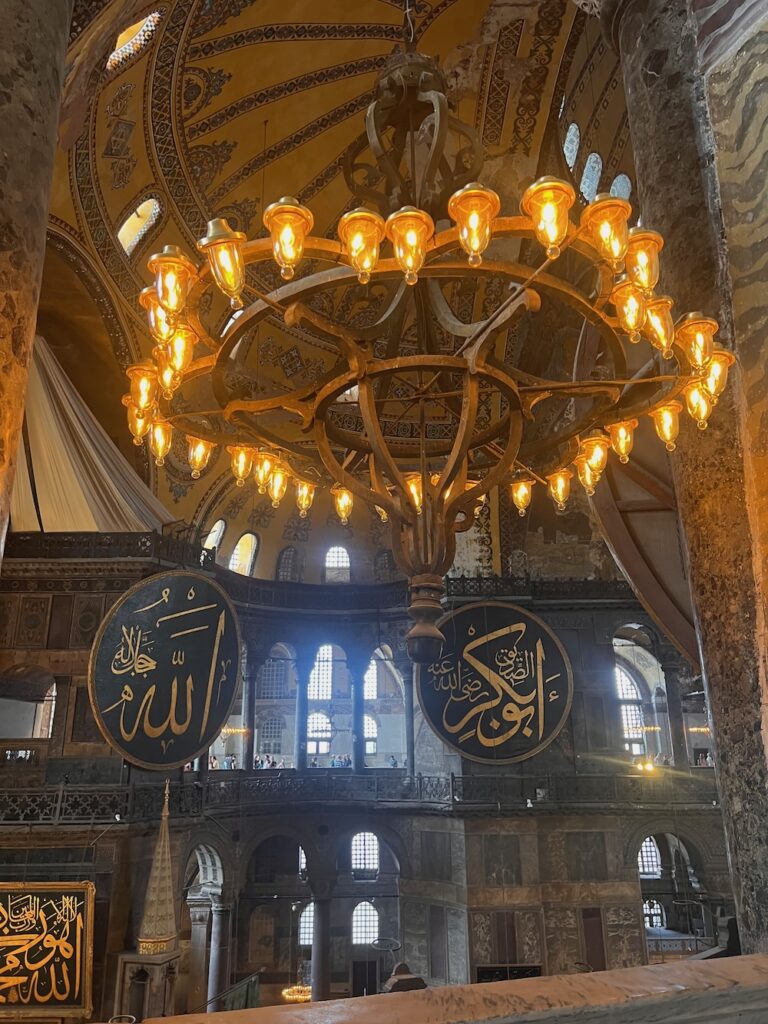 Inside the Hagia Sophia Mosque.  Calligraphy writing in gold and black plaques with an elegant chandelier.