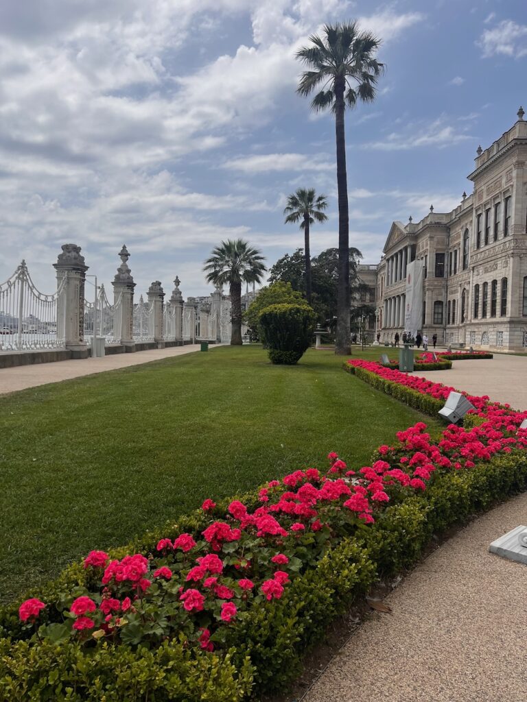 Manicured grass with red flowers, trees in the background and elegant fence at the Dolmabahçe Palace. 