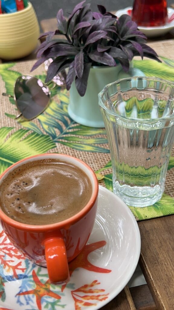 Orange cup of Turkish coffee and small glass of water. With purple flowers on the table. Asian Side of Istanbul tour.